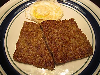 Two slices of fried goetta on a plate with an egg